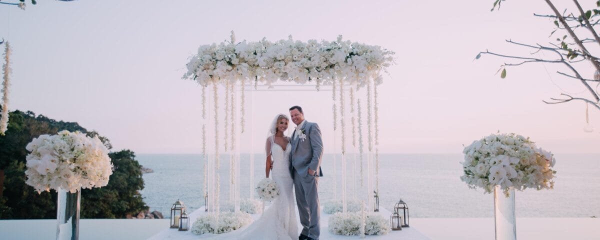 Wedding ceremony beneath a white floral arch overlooking the ocean