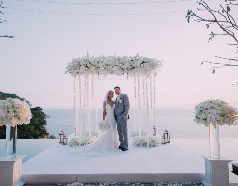 Wedding ceremony beneath a white floral arch overlooking the ocean
